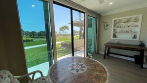 A spacious room with a large sliding glass door leading to a patio, a round marble table, and a bench. - Watch the sunset from you screened in lanai in this 2bd/2ba Condo (Sarasota)