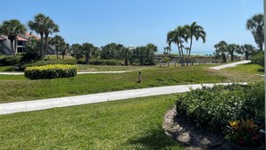 A landscaped area with a pathway, palm trees, and a view of the ocean. - Watch the sunset from you screened in lanai in this 2bd/2ba Condo (Sarasota)