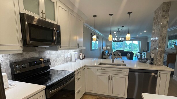 A modern kitchen with white cabinetry, stainless steel appliances, and pendant lighting. - Watch the sunset from you screened in lanai in this 2bd/2ba Condo (Sarasota)