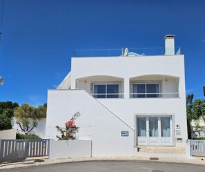 A modern two-story building with a white facade, large windows, and a balcony.