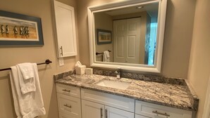 A bathroom with a large mirror, white cabinets, a granite countertop, and a framed picture on the wall. - Lovely Beach front 2Bd/2Bath Condo (Sarasota)