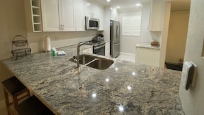 A kitchen with white cabinets, a stainless steel sink, a microwave, and a refrigerator. - Lovely Beach front 2Bd/2Bath Condo (Sarasota)