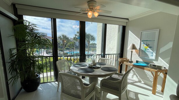 A balcony with a table and chairs, a potted plant, and a view of a pool and palm trees. - Lovely Beach front 2Bd/2Bath Condo (Sarasota)
