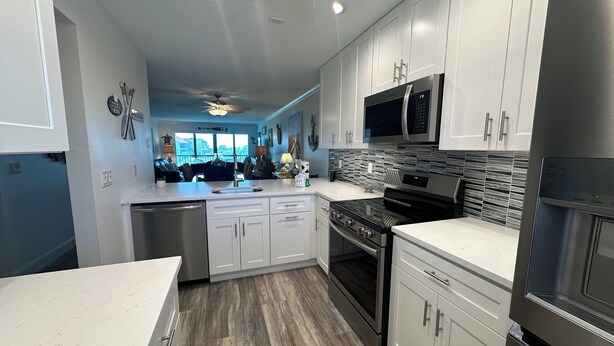 A modern kitchen with white cabinets, stainless steel appliances, and a wooden floor. - Enjoy beautiful sunset views (Sarasota)