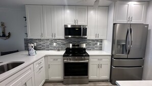 A modern kitchen with white cabinets, a stainless steel refrigerator, a microwave, and a stove. - Enjoy beautiful sunset views (Sarasota)