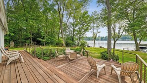 A wooden deck with outdoor furniture, a view of a lake, and a grassy area with trees.