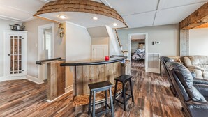 A spacious living area with a wooden bar, two stools, a leather sofa, and a staircase leading to another level.