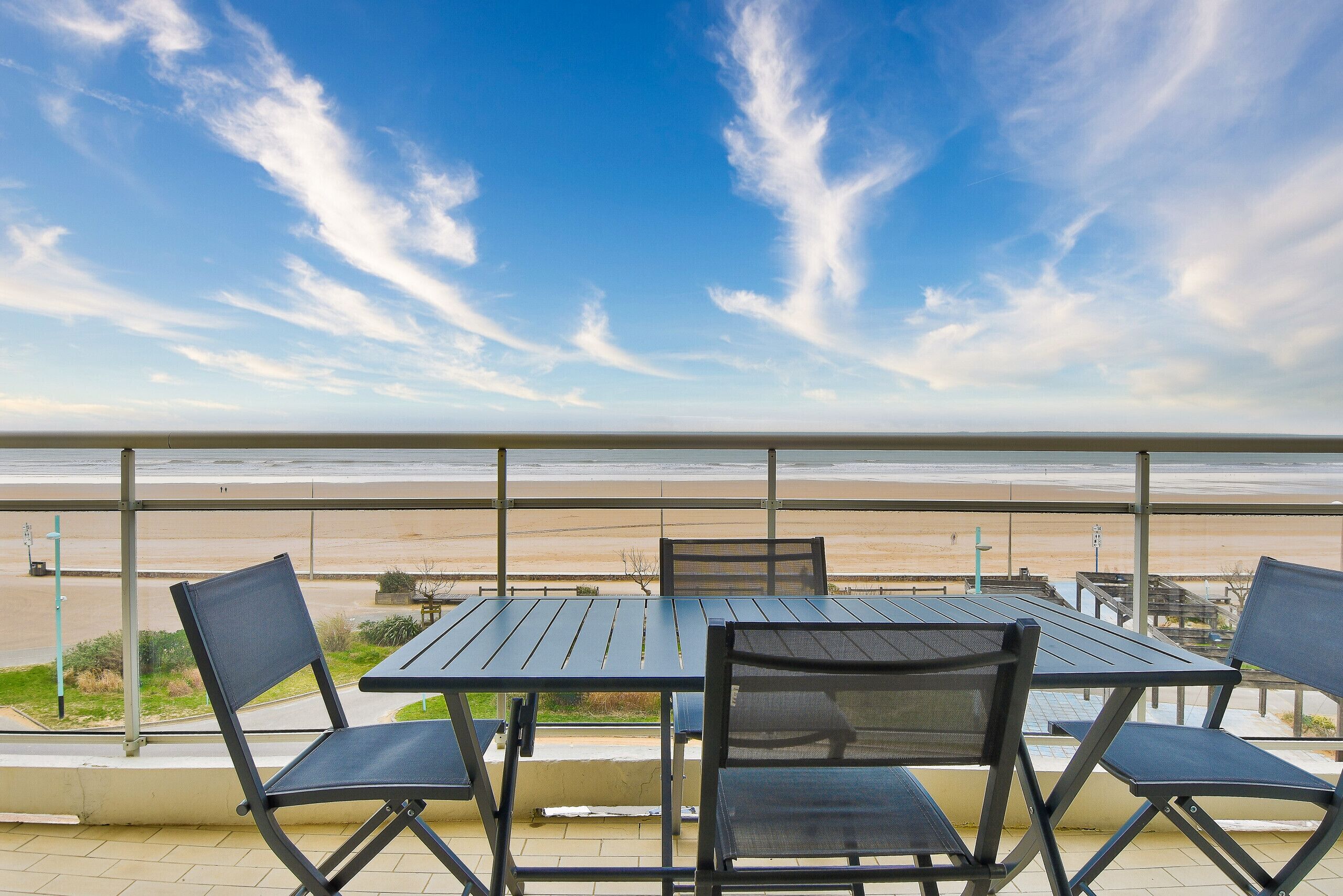 A balcony with a table and chairs overlooking a beach.