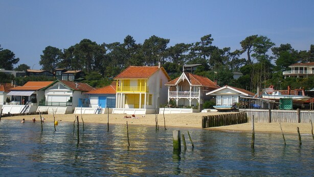 Una zona costera con casas coloridas, una playa arenosa y una masa de agua tranquila.
