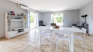 Una sala de estar moderna con una mesa de comedor blanca, sillas, un sofá y una estantería.