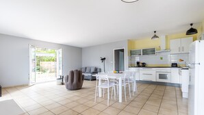 Una cocina moderna con armarios blancos, una zona de comedor con sillas blancas y un sofá gris.