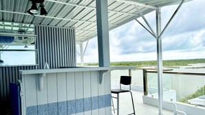 A covered outdoor area with a bar and a chair, overlooking a body of water and greenery.