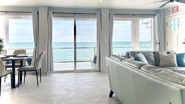 A spacious living area with a large sliding glass door leading to a balcony overlooking the sea.
