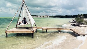 A wooden platform extending into clear turquoise water with a hammock and a person relaxing.