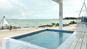 A beachside pool with a wooden deck, a hammock, and a view of the ocean.