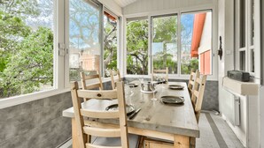 A dining area with a wooden table and chairs, large windows, and a view of trees and buildings. - 150m from Betey Beach, house for 6 (Andernos-les-Bains)