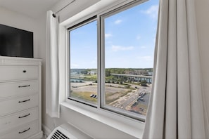 A room with a large window, a white dresser with drawers, and a view of a bridge and buildings.
