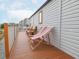 Una terraza de madera con dos sillas de madera y una hamaca a rayas.
