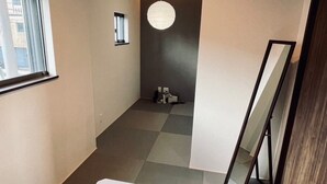 Ein moderner, minimalistischer Raum mit großem Fenster, weißem Tisch, einer hängenden Leuchte und einem an der Wand lehnten Spiegel.