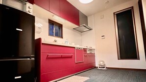 Eine kleine Küche mit roten Schränken, einem schwarzen Kühlschrank, einem Fenster und einem Deckenventilator.