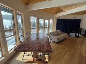 A spacious room with a large wooden dining table, a sofa, and large windows offering a view of a snowy landscape.