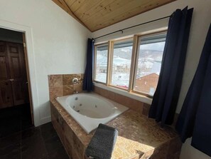 A bathroom with a large bathtub, a window with curtains, and a view of a snowy landscape.