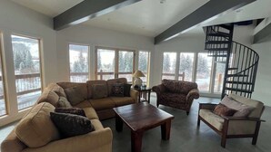 A spacious living room with a large window, a wooden coffee table, and a spiral staircase. - Cliff House - Newly remodel home with amazing view (Crested Butte)