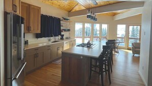 A modern kitchen with wooden cabinets, a central island, and a dining area with chairs. - Cliff House - Newly remodel home with amazing view (Crested Butte)