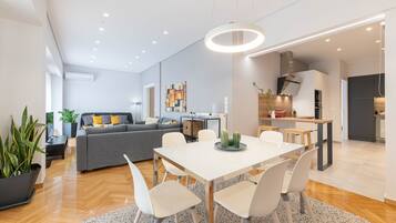 A modern living space with a dining area, kitchen, and a grey sofa with yellow cushions.
