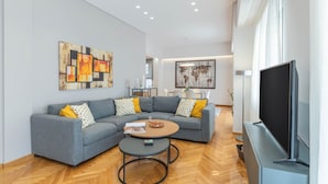 A modern living room with a grey sectional sofa, a coffee table, and a flat-screen TV. - The HostMaster Cosmopolitan Downtown Scent (Αθήνα)