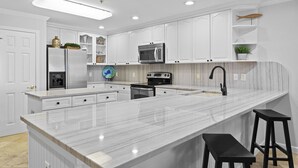 Eine moderne Küche mit weißen Schränken, einer Marmorarbeitsplatte, einem eingebauten Backofen, einer Mikrowelle und einem Waschbecken mit einem schwarzen Wasserhahn.