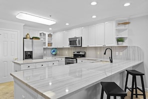 A modern kitchen with white cabinetry, a marble countertop, a built-in oven, a microwave, and a sink with a black faucet.