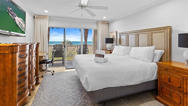 Ein Hotelzimmer mit einem großen Bett, einem Deckenventilator, einem Schreibtisch mit Stuhl, einem Fernseher und Blick auf den Ozean.