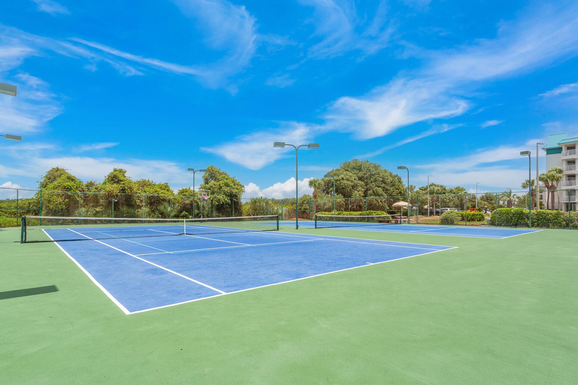 A tennis court with a net, surrounded by greenery and trees.