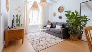A living room with a grey sofa, a wooden side table, a woven rug, and a large plant.