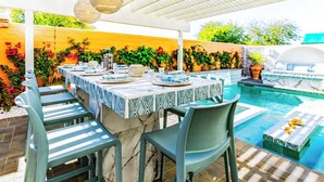 Une terrasse extérieure avec une piscine, un espace repas couvert avec une table dressée pour quatre personnes, et un coin salon.