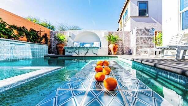 Une piscine dont le carrelage présente des motifs géométriques, un espace détente avec un canapé blanc et des plantes en pot.