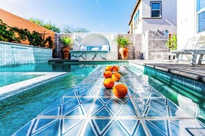 A swimming pool with geometric tile patterns, a seating area with a white couch, and potted plants. - Santorini Greek Villa (Indio)