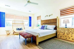 A bedroom with a bed, a chair, a bench, and a window with blinds. - Santorini Greek Villa (Indio)