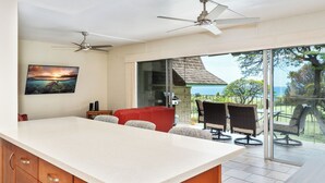 A spacious kitchen with a large island, a dining area with outdoor seating, and a view of the ocean. - Summer Deal Kona Vacation Condo with Ocean Views Lanai and Resort Pool (Kailua-Kona)