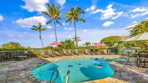 A swimming pool with lounge chairs and umbrellas, surrounded by palm trees and a stone deck. - Summer Deal Kona Vacation Condo with Ocean Views Lanai and Resort Pool (Kailua-Kona)