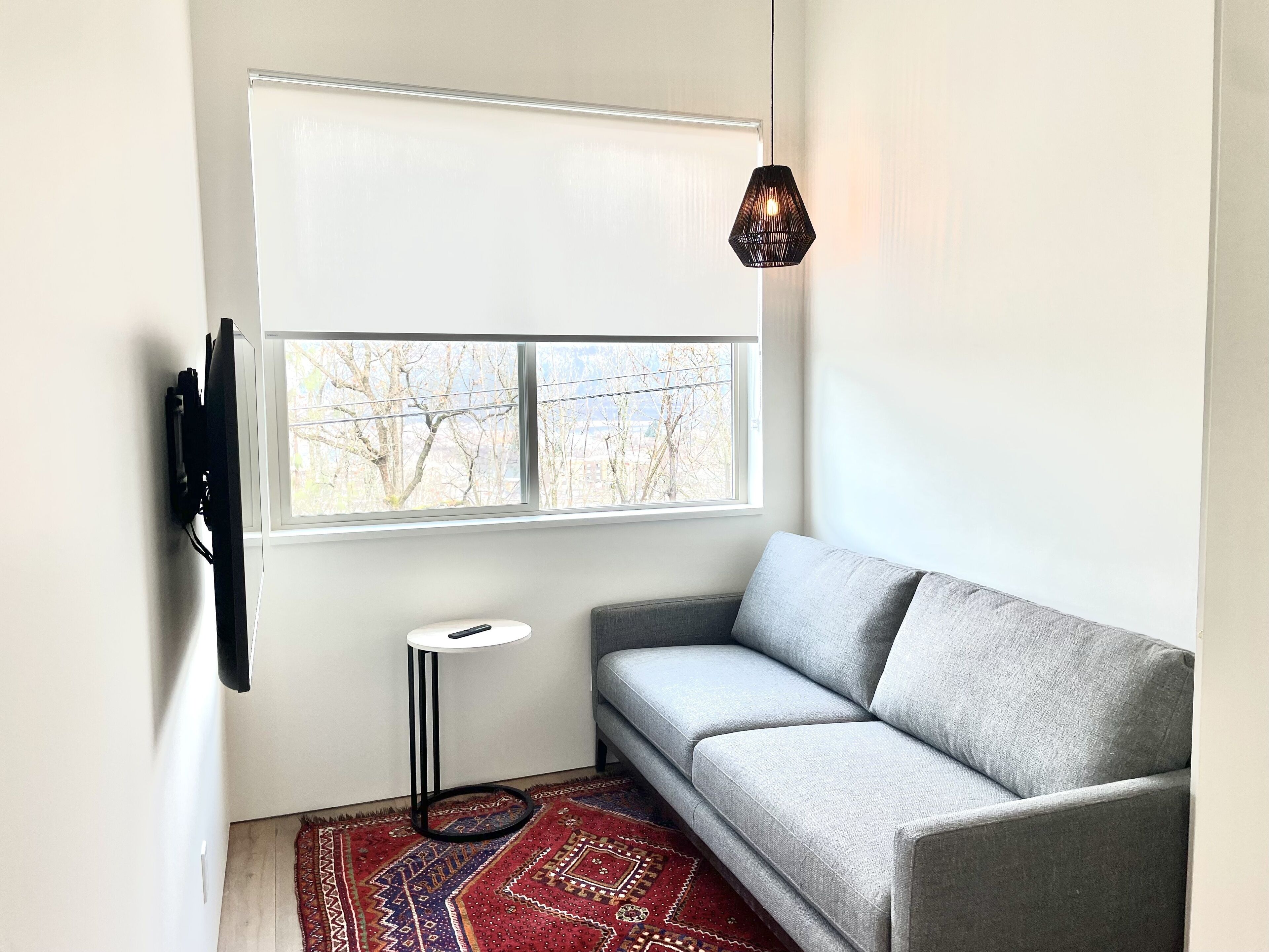 Un salon moderne avec un canapé gris, un tapis à motifs, une petite table d’appoint et un luminaire suspendu.