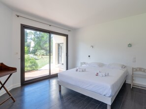Un dormitorio con cama, escritorio y puerta corrediza de vidrio que da a un jardín.
