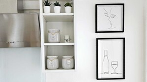 A kitchen with a white cabinet containing jars labeled 'tea,' 'coffee,' and 'bread.' There are two framed line drawings on the wall depicting a face and a wine bottle with a glass. - SEAVIEW apartment (Littlehampton)