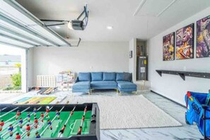 A modern living room with a foosball table, a blue sofa, and artwork on the wall. - ~Coastal Gameday~ Sports, Beach, OWA & Shopping! (Foley)