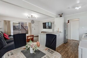 Moderni olohuone, jossa on sohva, ruokapöytä ja tuoleja. Siellä on myös keittiöalue, jossa on jääkaappi ja televisio.