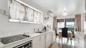 Une cuisine moderne avec des armoires blanches, une cuisinière encastrée et une fenêtre agrémentée d’un rideau à motifs de fruits.