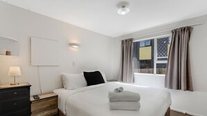 Une chambre d’hôtel avec un lit, une table de chevet, une lampe, une fenêtre avec des rideaux et une vue sur l’extérieur.