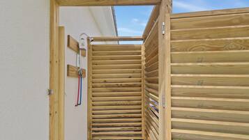 Une structure en bois dotée d’un toit à lattes, qui pourrait être un sauna ou un espace douche, avec des tuyaux apparents et un accessoire métallique fixé au mur.