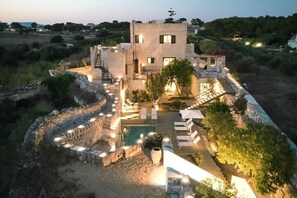 A modern villa with a swimming pool, outdoor seating, and a stone wall surrounding the property.